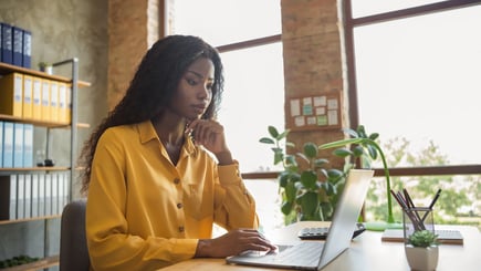 Professional woman working on a laptop in a bright office with plants and shelves