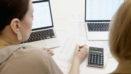  Two people analyzing data with laptops, printed charts, and a calculator