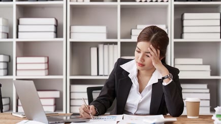 Stressed businesswoman reviewing documents at her desk with a laptop and coffee cup