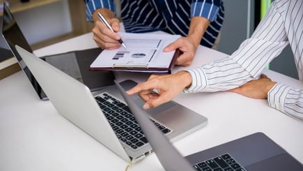 Two people reviewing data on a clipboard and laptop, discussing graphs and charts during a meeting