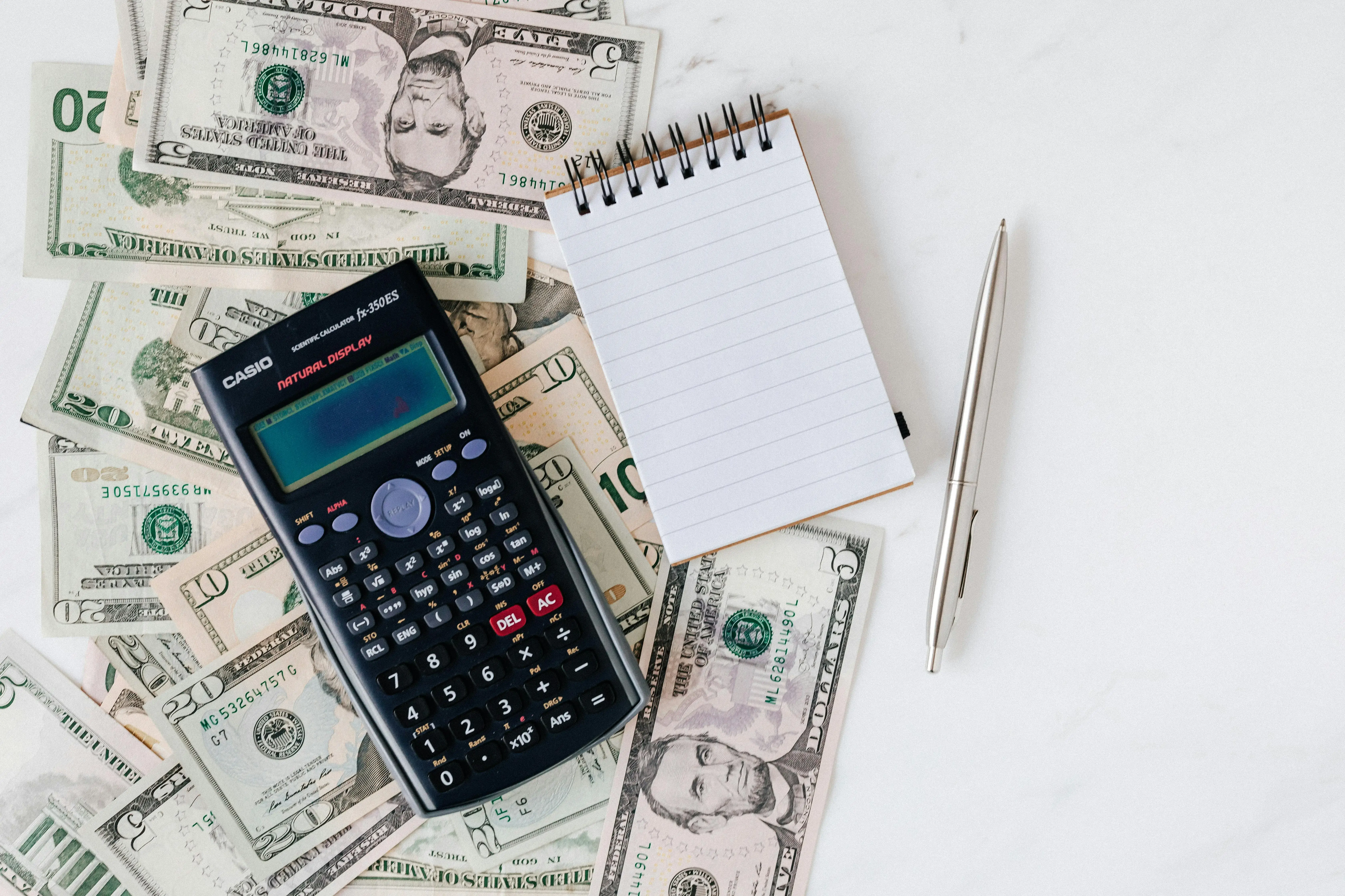 calculator notebook and pen on dollar bills