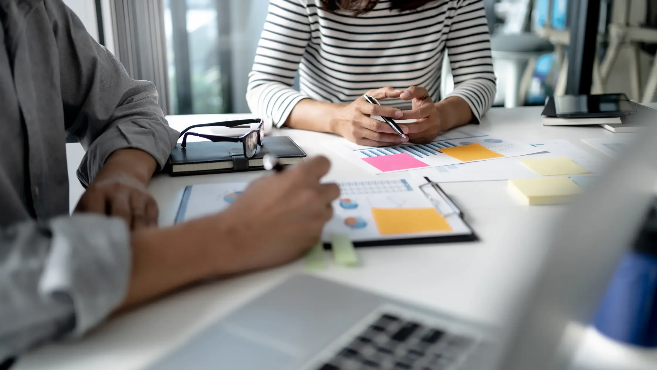 Two people reviewing documents with charts and sticky notes during a business meeting at a desk
